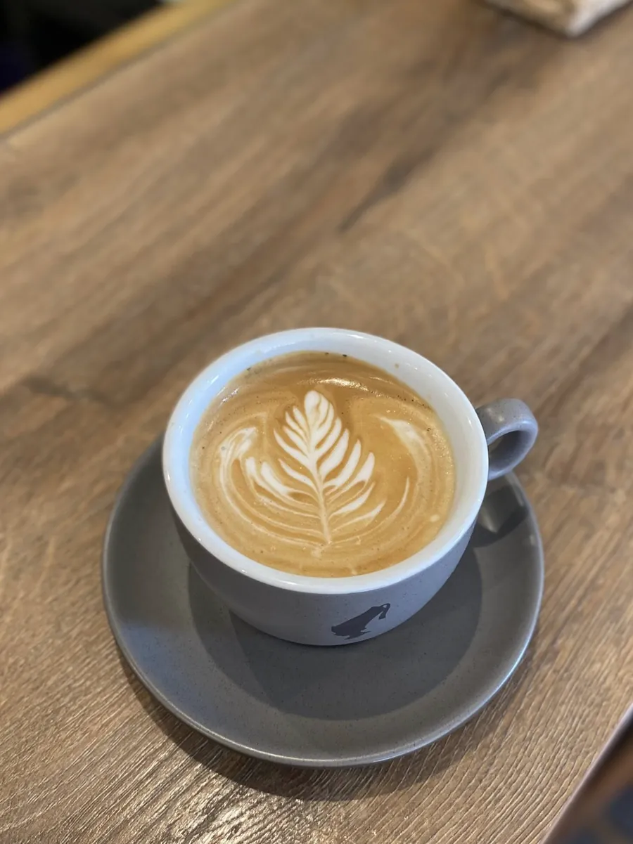Šálek kávy s latte artem ve tvaru listu na dřevěném stole
